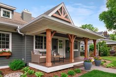 a gray house with a covered porch and chairs on the front lawn, surrounded by greenery