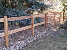 the fence is made of wood and has rocks on it, along with pine trees