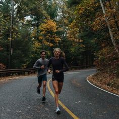 two people are running down the road in the fall or early autumn time, with trees and foliage behind them