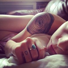 a woman laying on top of a bed with tattoos on her arm and chest next to a brown leather couch