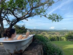 a woman sitting in a bathtub holding a glass of wine and looking out over the countryside