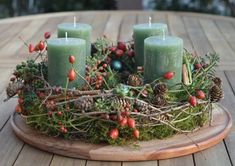 three candles are placed in a wreath with pine cones, berries and evergreen needles on a wooden table