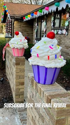 two cupcakes sitting on top of brick blocks in front of a house with flags