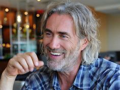 a man with grey hair and beard smiles at the camera while sitting in a restaurant