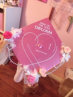 a pink graduation cap that says made in the shape of a heart with flowers on it