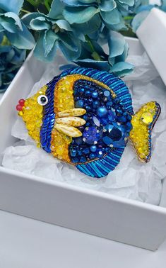 a blue and yellow fish sitting on top of a white box next to some flowers