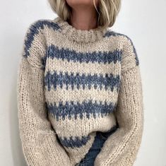 a woman with blonde hair wearing a blue and white striped knitted sweater, sitting on the ground