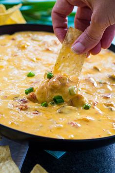 a hand dipping a tortilla chip into a bowl of quesadilla