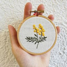 a hand holding a small embroidered yellow flower