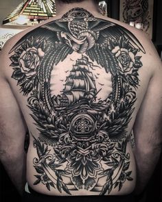 a man's back with an eagle and ship tattoo on it