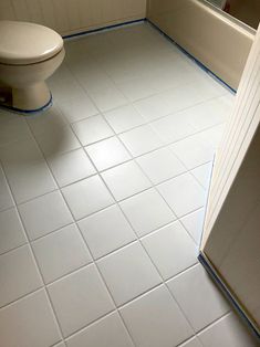 a white toilet sitting in a bathroom next to a bath tub and shower stall with blue tape on the floor