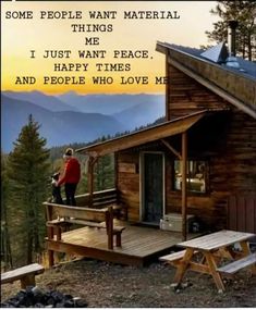 a person standing on top of a wooden porch next to a small cabin with mountains in the background