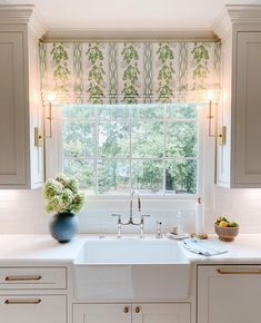 a kitchen with white cabinets and a sink in front of a window that has green leaves on it