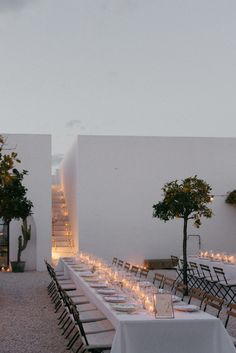 an outdoor dining area with long tables and chairs, lit up by candles on each table