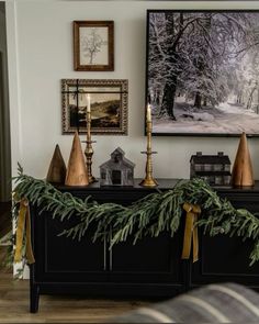 a christmas mantle decorated with evergreen garland and gold candlesticks in front of a photograph on the wall