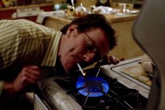 a man bending over to look at a blue flame on a stove top burner