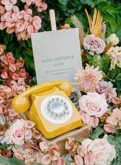 an old yellow phone sitting on top of a box surrounded by flowers and greenery