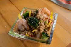 a glass dish filled with shrimp, broccoli and other vegetables on top of a wooden table