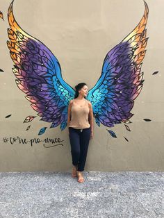 a woman standing in front of a wall with wings painted on it