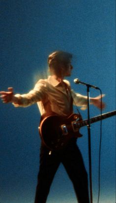 a man standing in front of a microphone with his arms out and holding a guitar