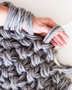 a hand is crocheting the ends of a chunky blanket