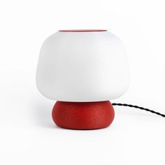 a red and white lamp sitting on top of a wooden table next to a black cord