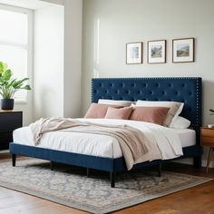 a bed with blue headboard and pillows in a white room next to a window