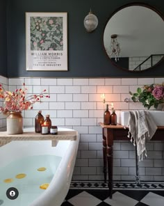 a bath room with a tub a mirror and flowers in vases on the counter