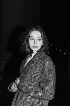 black and white photograph of a woman in a coat standing with her arms crossed, looking at the camera