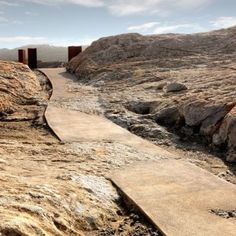 a path leading to two gates in the middle of a rocky area with dry grass and dirt