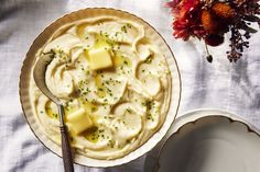 a bowl of mashed potatoes next to a plate with butter and herbs on it