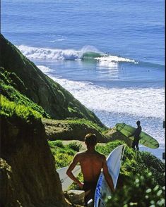 two surfers are walking up the hill to the beach with their surfboards in hand