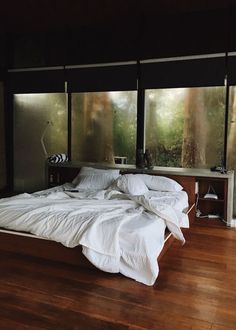 a large bed sitting on top of a hard wood floor next to two tall windows