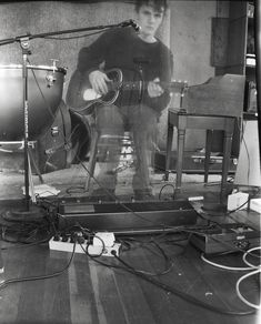 a man standing in front of a guitar on top of a wooden floor next to two microphones