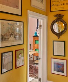 an entry way with yellow walls and pictures on the wall, framed in gold frames