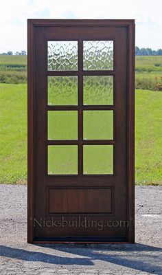 a wooden door with glass panels in front of a grassy field on a sunny day