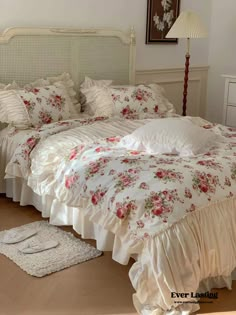 a white bed with pink flowers on it in a bedroom next to a dresser and lamp