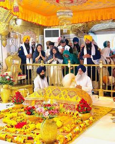 men in yellow turbans sitting on a bed surrounded by flowers and other people