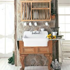 an old fashioned kitchen sink with dishes on the shelf above it and sunflowers