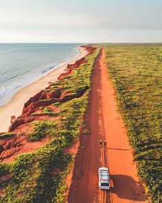 a truck driving down a dirt road next to the ocean on top of green grass