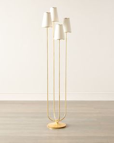 three brass floor lamps with white shades on the top and bottom, in front of a wall