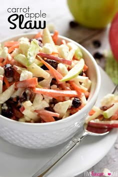 a white bowl filled with carrots, apple slices and cranberries next to an apple