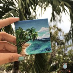 a hand holding up a small card with palm trees on the beach in the background