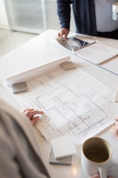 three people sitting at a table with blueprints on it and coffee mug in front of them