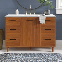 a bathroom with blue walls and white counter tops, wooden cabinetry, and round mirror