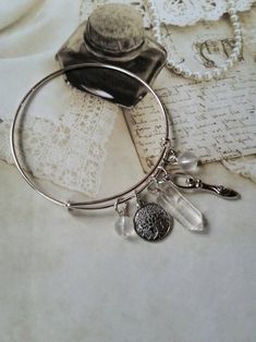 This cute silver-toned metal expandable charm bangle was made with Lammas, or Lughnasadh, in mind. It matches a Lammas themed prayer bead strand I recently made. It would also match most anything else, as well, since the stones used are clear. It's made with a silver-toned metal expandable bangle and features a gemstone point, silver-toned metal charms, and bead dangles. In the center is a small bullet-shaped clear Quartz pendulum point. It has two silver-toned metal charms. One is a Goddess and Bead Dangles, Goddess Jewelry, Metal Charms, Stainless Steel Bangles, A Goddess, Cameo Pendant, Charm Bangle, Metal Charm, Prayer Beads