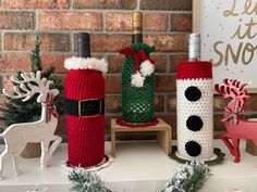 three knitted wine bottles sitting on top of a table next to a christmas tree