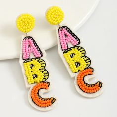 Add some fun and color to look with our fun Beaded ABC Earrings! In playful pink, yellow, and orange hues, these lightweight earrings are perfect for teachers and students alike! Details: Super lightweight at just 0.2 ounces Measures approximately 3 inches long x 3/4 inches wide Post backing Nickel-free Reverse side is a felt lining Trendy Yellow Earrings With Colorful Beads, Novelty Multicolor Earrings With Ear Wire, Trendy Yellow Beaded Dangle Earrings, Fun Yellow Earrings With Ear Wire, Playful Yellow Dangle Earrings, Trendy Yellow Beaded Earrings, Playful Multicolor Personalized Earrings, Playful Personalized Multicolor Earrings, Colorful Fun Beaded Earrings As Gift