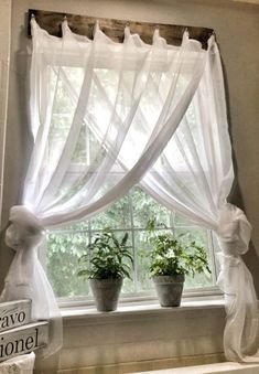 the window is decorated with white curtains and potted plants