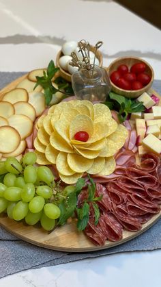 a platter with grapes, meats and cheese is displayed on a white tablecloth